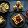 A stunning, dark, flat-lay photograph of a tasting menu made from transformed Thanksgiving leftovers, including a bowl of ramen, crispy arancini, a stuffing waffle, and a cranberry cocktail.