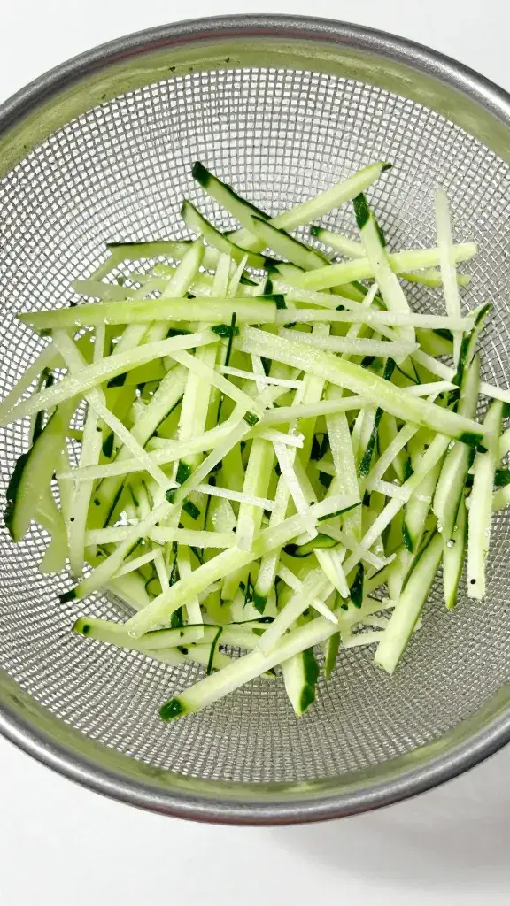 grated cucumber in fine-mesh sieve draining