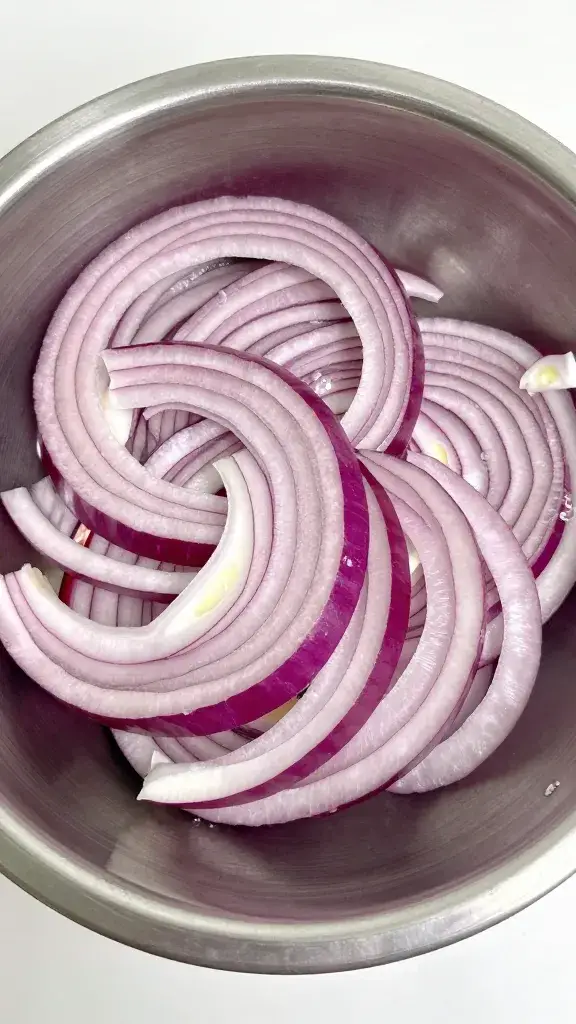 thinly sliced red onion ribbons in stainless steel bowl