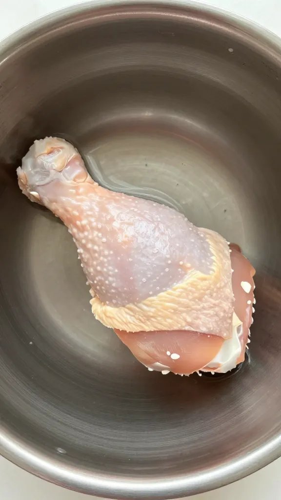 Stainless mixing bowl with single chicken thigh submerged