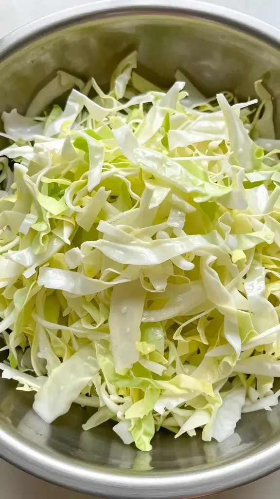 Stainless steel bowl of salted, draining shredded cabbage, closeup