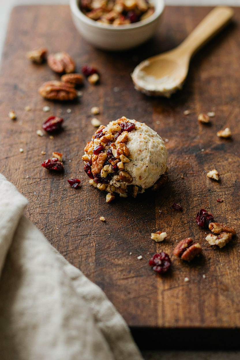 Cheese ball being rolled in chopped toasted pecans and dried cranberries
