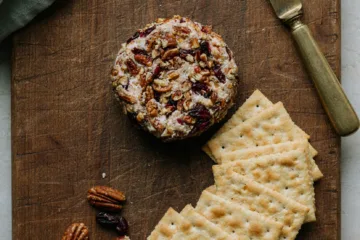 Cheese ball coated in pecans and cranberries on rustic board