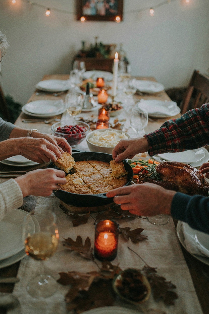 Thanksgiving table with cast iron skillet of golden cornbread in the center, family reaching for pieces