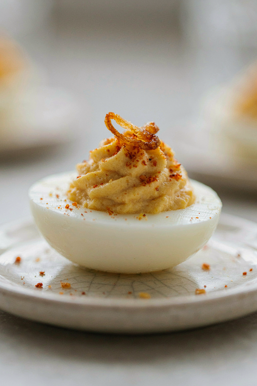Close-up of deviled egg half with perfectly piped filling, paprika dusted, crispy shallot topping