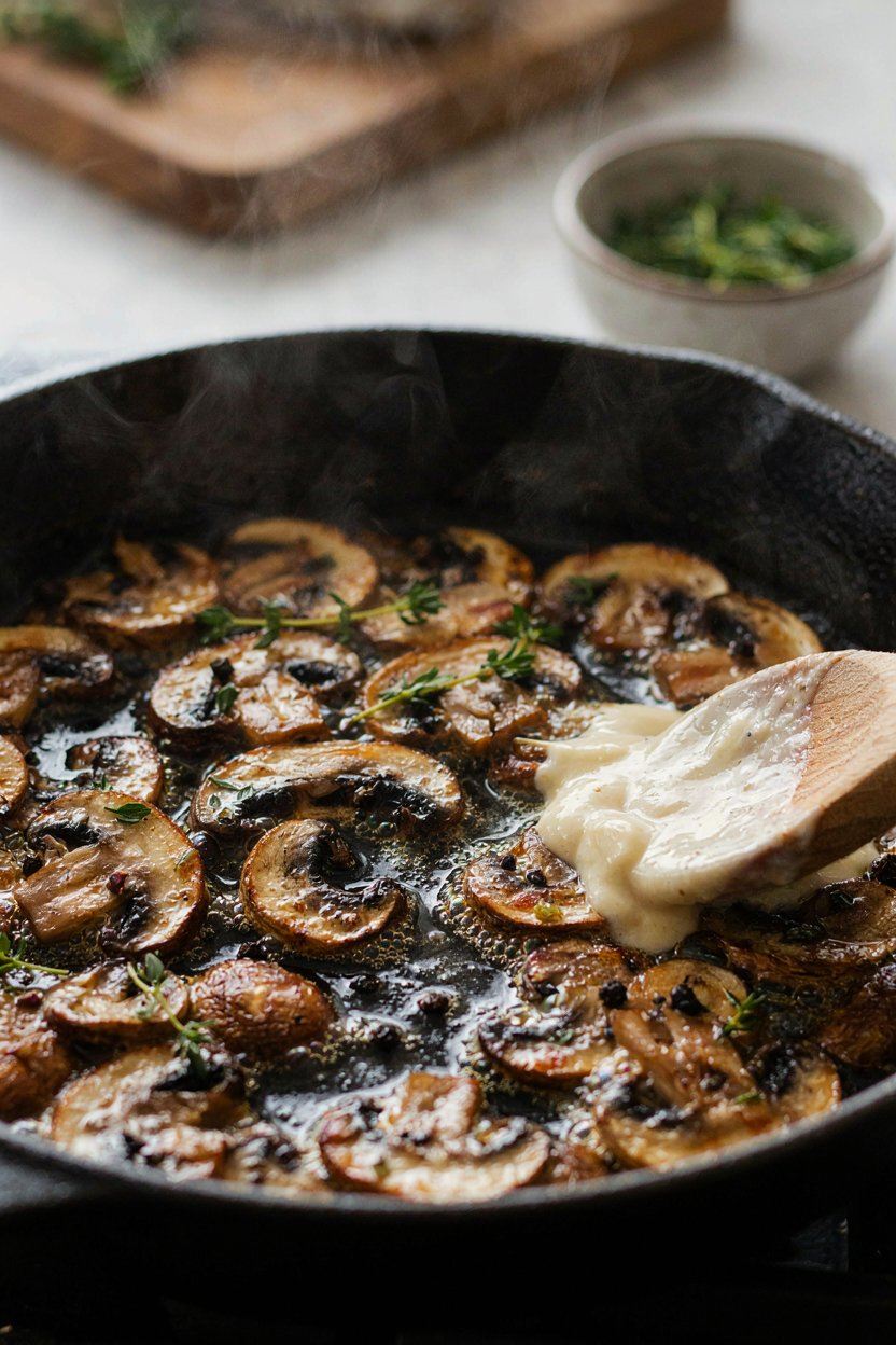 Mushrooms browning in large skillet, golden brown edges, butter sizzling, creamy sauce being stirred in