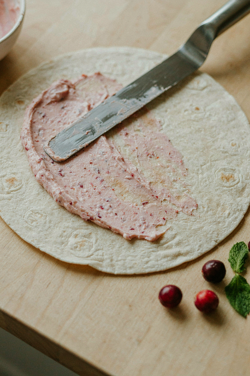 Pink cranberry cream cheese being spread onto flour tortilla
