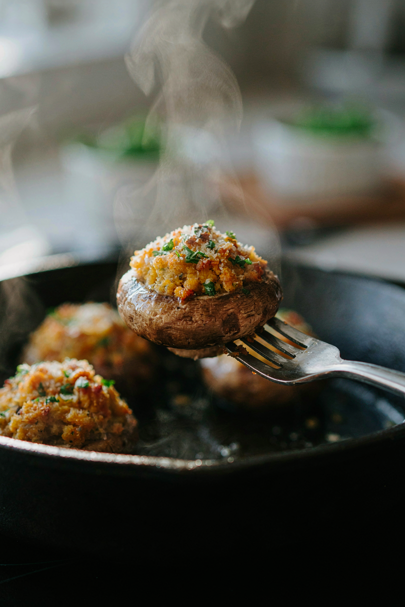Close-up of stuffed mushroom being lifted with fork, golden brown filling visible, steam rising
