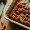 Corner of baking dish showing sweet potato filling under pecan streusel