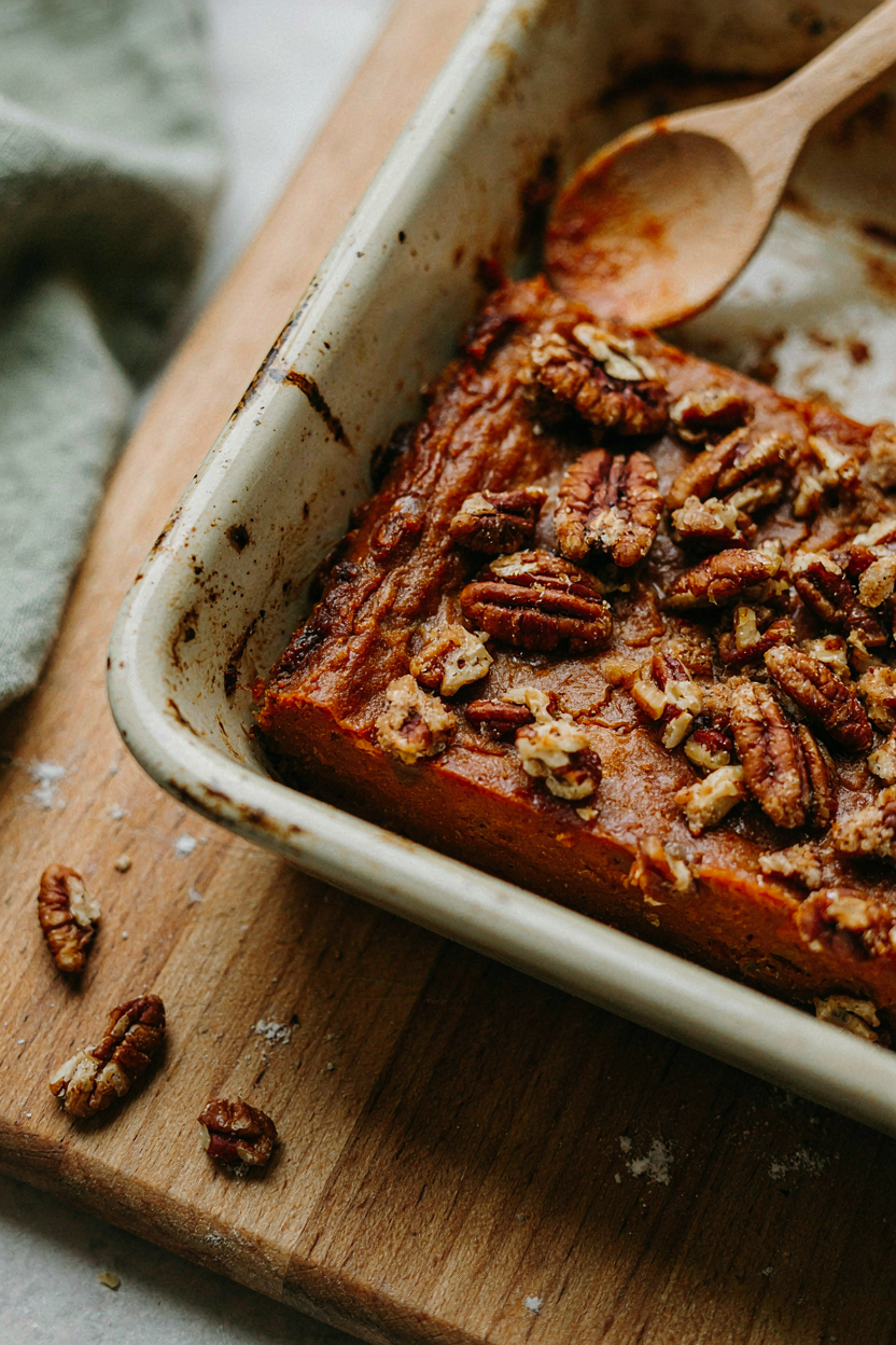 Corner of baking dish showing smooth orange sweet potato filling under craggy golden pecan streusel