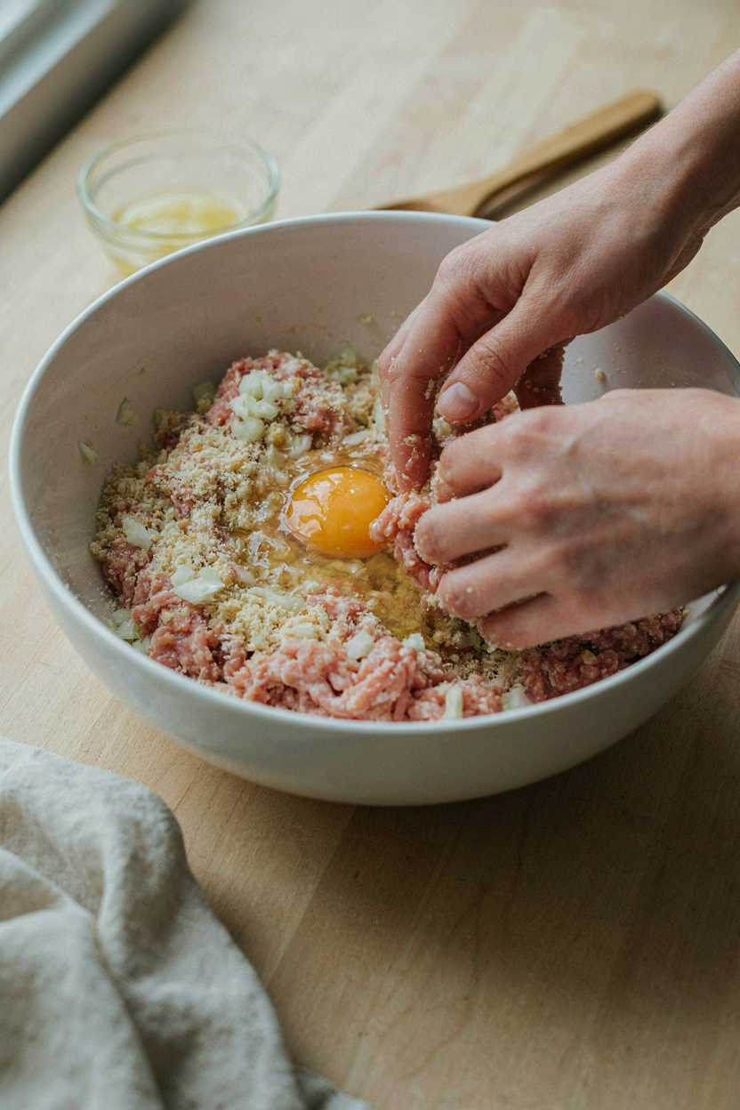Hands mixing ground turkey with breadcrumbs and grated onion